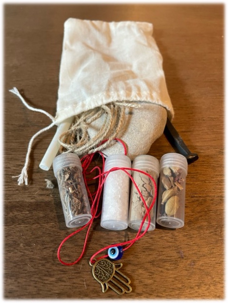 A picture of a monster hunting kit; a bag of string, chalk, an iron nail and a sone, vials of salt, ash, bessamim, and rue, and a hamsa on a red thread.